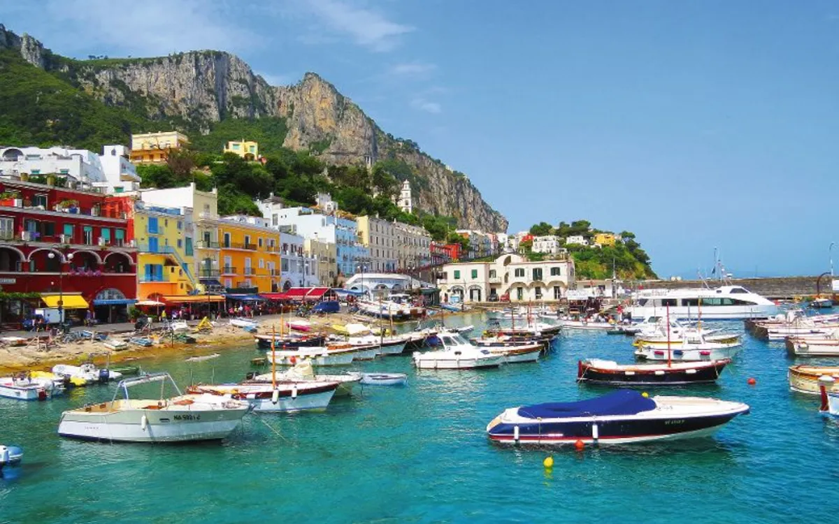 Boote im Hafen vor farbigen Gebäuden und Klippen auf der Insel Capri.