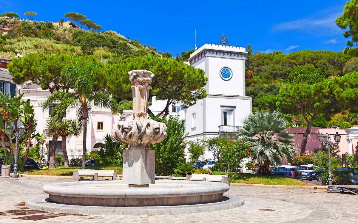 Brunnen auf dem Stadtplatz mit Gebäuden und Bäumen im Hintergrund.