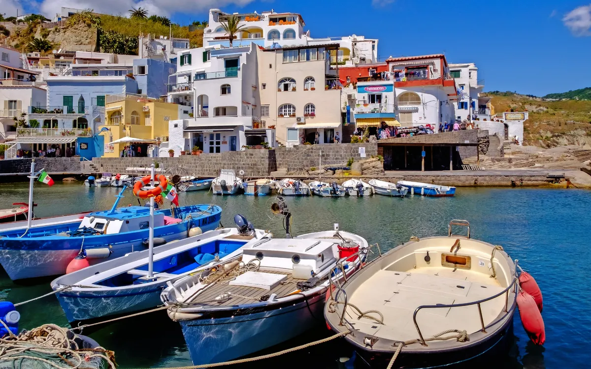 Fischerboote im Hafen von Sant'Angelo, Ischia, mit bunten Häusern im Hintergrund.