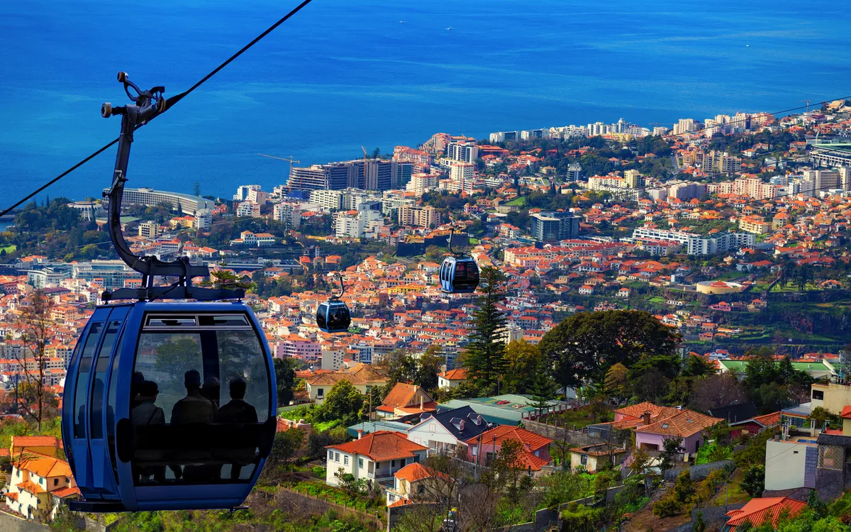 Seilbahn über Stadt mit Meer im Hintergrund.