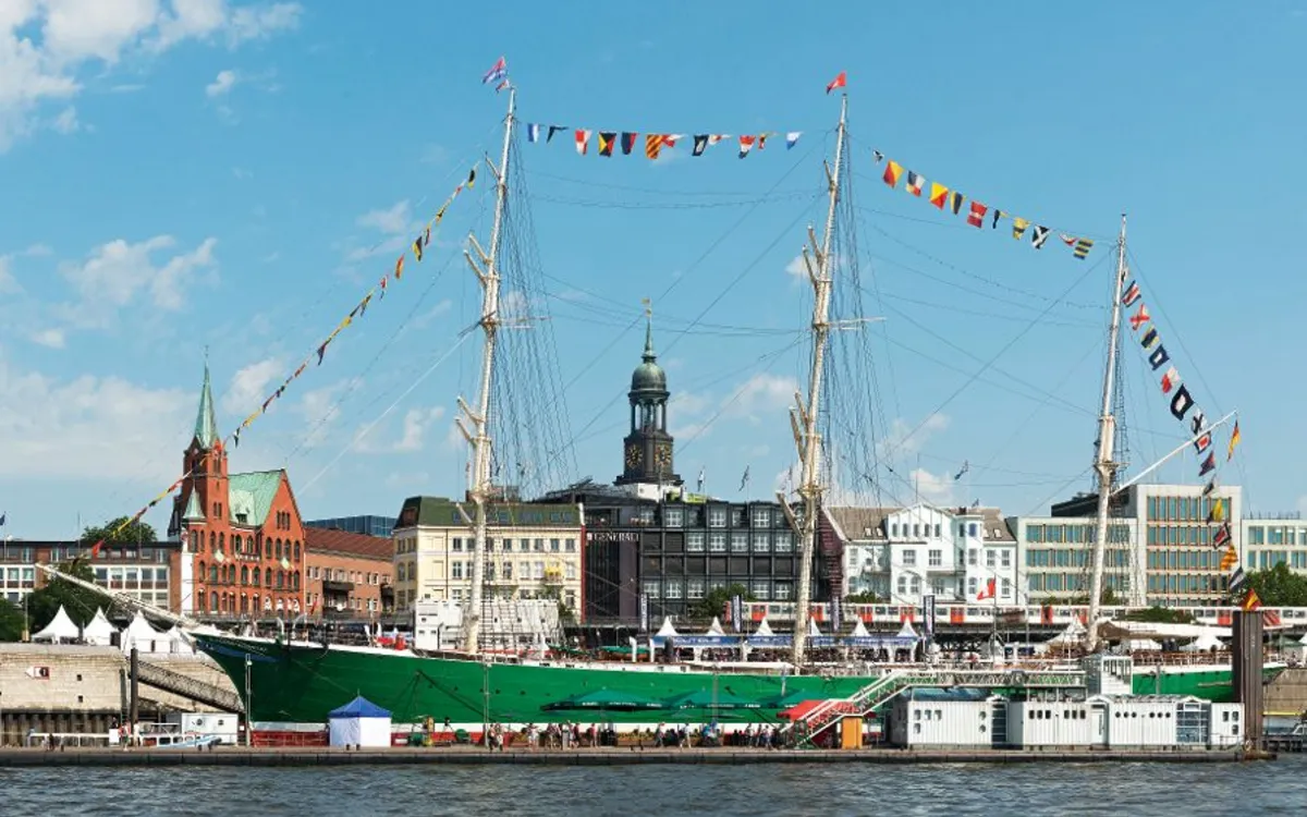 Segelschiff im Hafen vor historischer Stadtkulisse bei klarem Himmel.