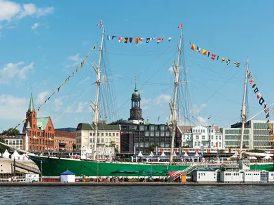 Segelschiff im Hafen vor historischer Stadtkulisse bei klarem Himmel.