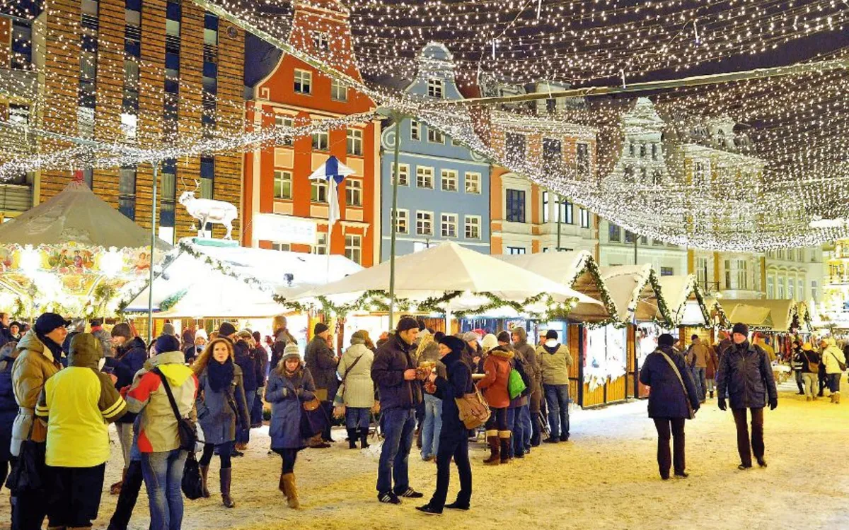 Weihnachtsmarkt mit Ständen und Lichtern, Menschen schlendern im Schnee.