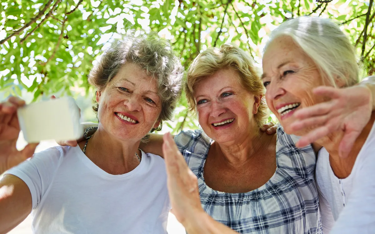Seniorinnen machen im Freien ein fröhliches Selfie mit einem Smartphone.