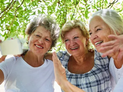 Seniorinnen machen im Freien ein fröhliches Selfie mit einem Smartphone.