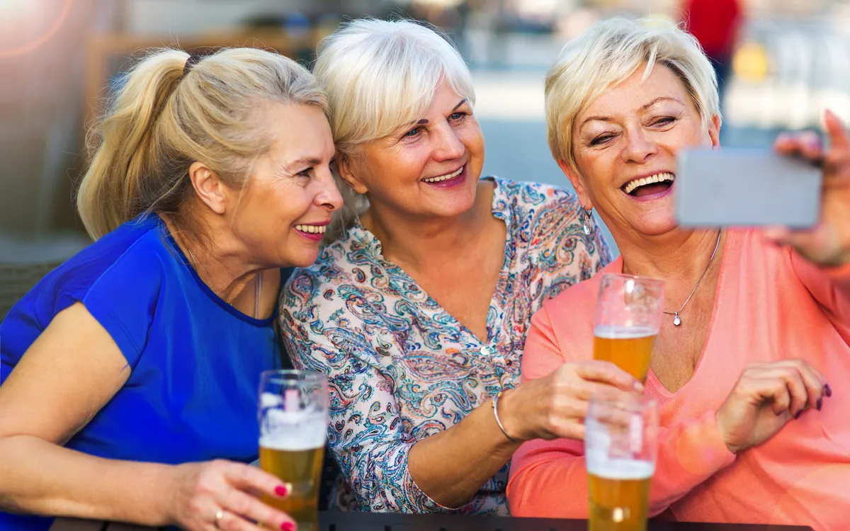 Lachende ältere Frauen trinken Bier in einer Kneipe im Freien.