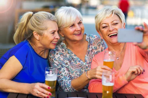 Lachende ältere Frauen trinken Bier in einer Kneipe im Freien.