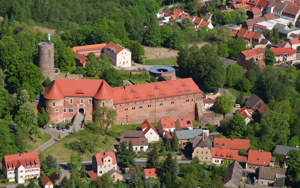 Luftbild der Burg Eisenhardt in Bad Belzig umgeben von grüner Landschaft.