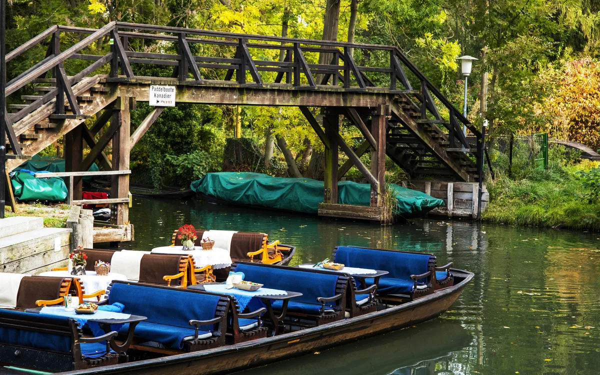 Boot für Kahnfahrt im Spreewald unter Holzbrücke, umgeben von Bäumen.