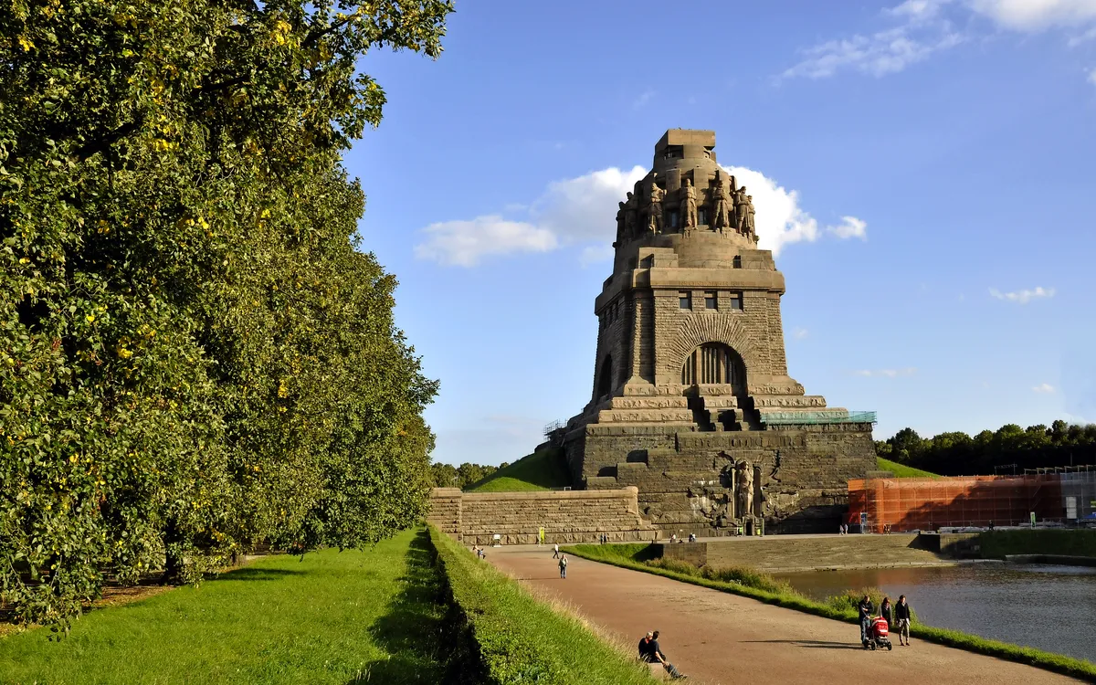 Leipziger Völkerschlachtdenkmal bei sonnigem Wetter mit Spaziergängern im Vordergrund.