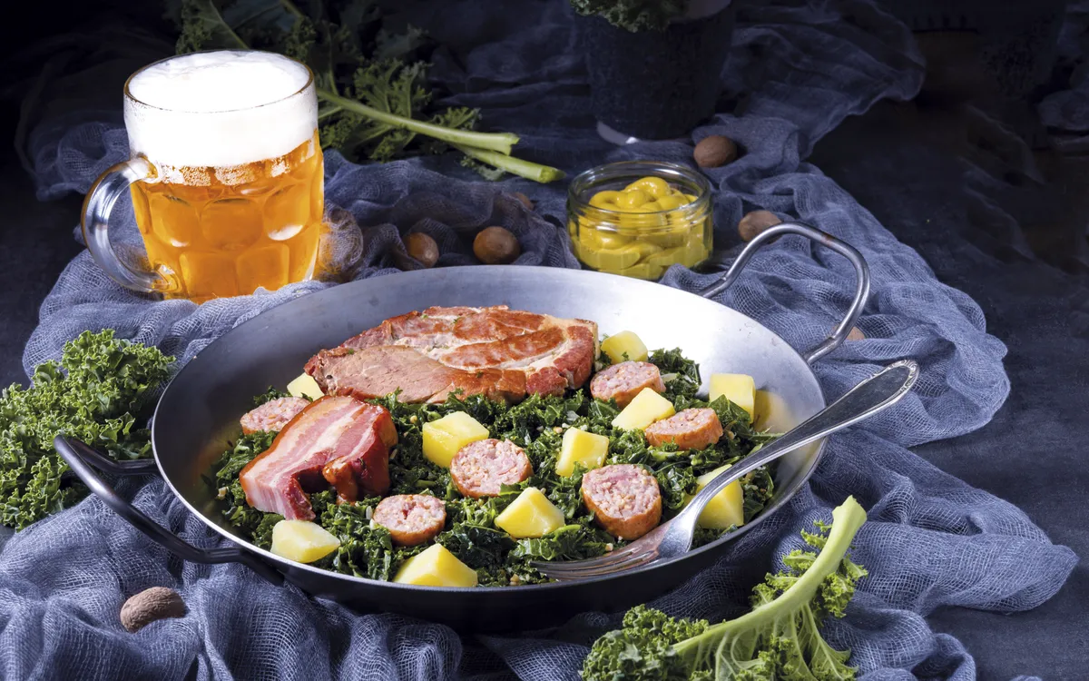 Grünkohlpfanne mit Pinkel, Kassler und Kartoffeln auf einem Tisch.