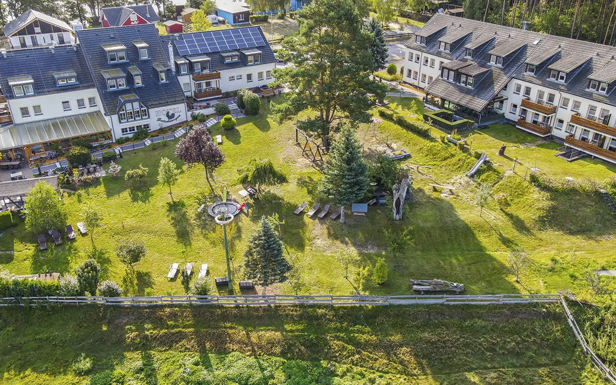 Luftaufnahme eines Hotelkomplexes mit Garten und Bäumen im Sommer.