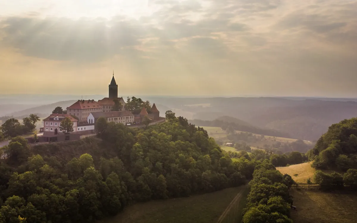 Leuchtenburg auf bewaldetem Hügel im Sonnenuntergang.