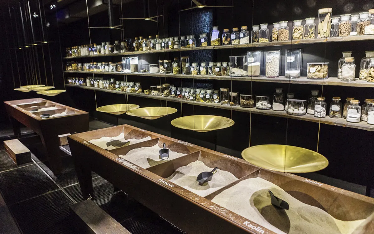 Ausstellung mit Sandbehältern und Regalen voller Gläser in einem Museum.