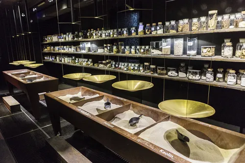 Ausstellung mit Sandbehältern und Regalen voller Gläser in einem Museum.