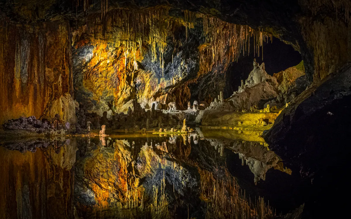 Saalfelder Feengrotte mit bunten Tropfsteinhöhlen und reflektierendem Wasser im Vordergrund.