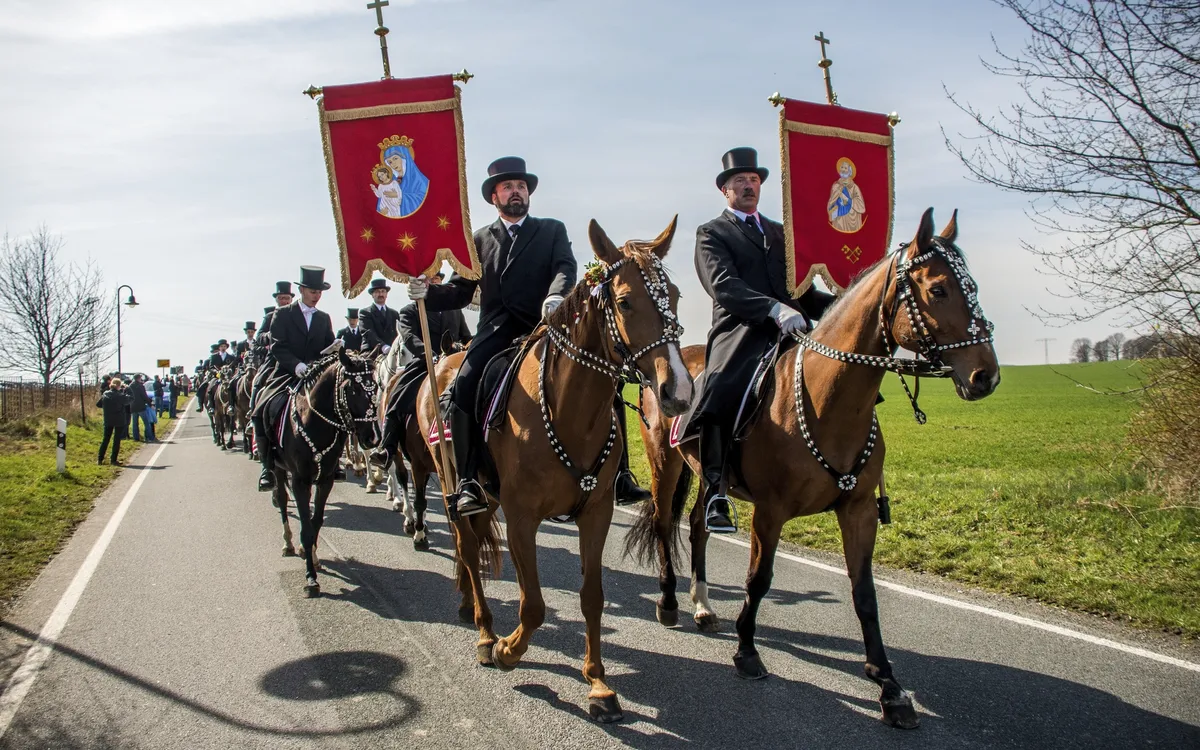 Reiter in traditioneller Tracht mit Fahnen bei einer Prozession.
