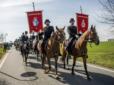 Reiter in traditioneller Tracht mit Fahnen bei einer Prozession.