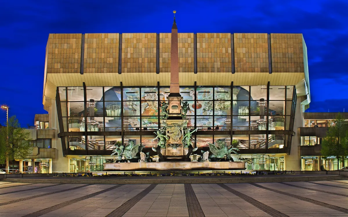 Konzerthaus mit moderner Glasfassade und Skulpturen im Vordergrund bei Nacht.