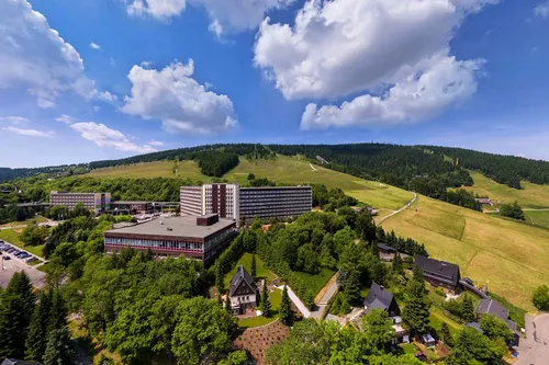 Hotelgebäude umgeben von grüner Landschaft und bewaldeten Hügeln.