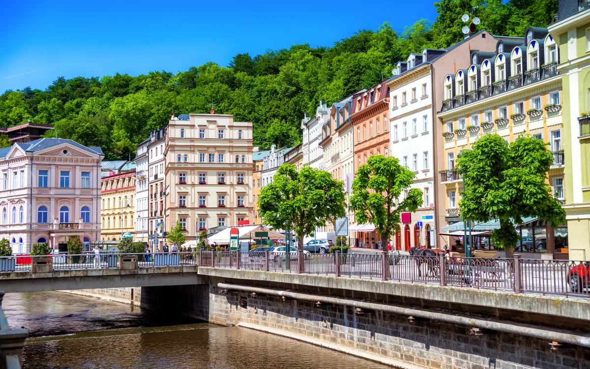 Bunte Häuser und Fluss in Karlsbad, umgeben von grünen Bäumen.
