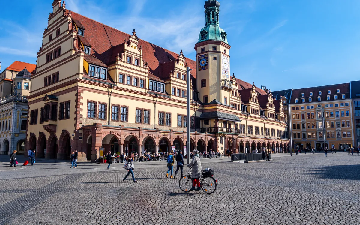 Historisches Gebäude mit Turm auf großem, belebtem Platz bei blauem Himmel.