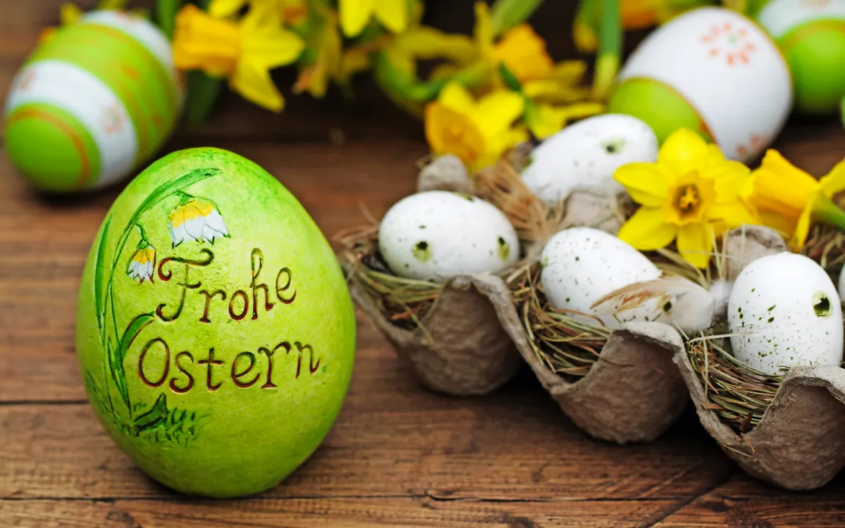 Grünes Osterei mit "Frohe Ostern" und gelbe Narzissen auf Holztisch