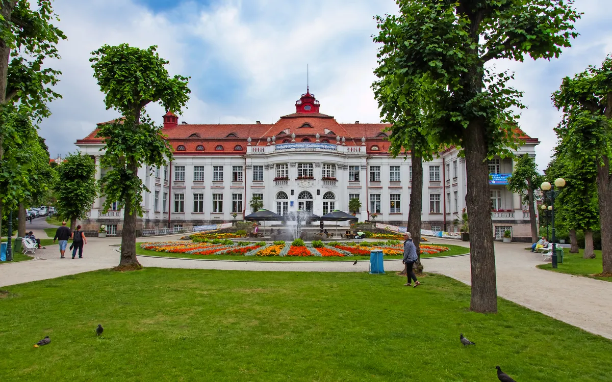 Historisches Gebäude mit Brunnen und Park im Vordergrund.