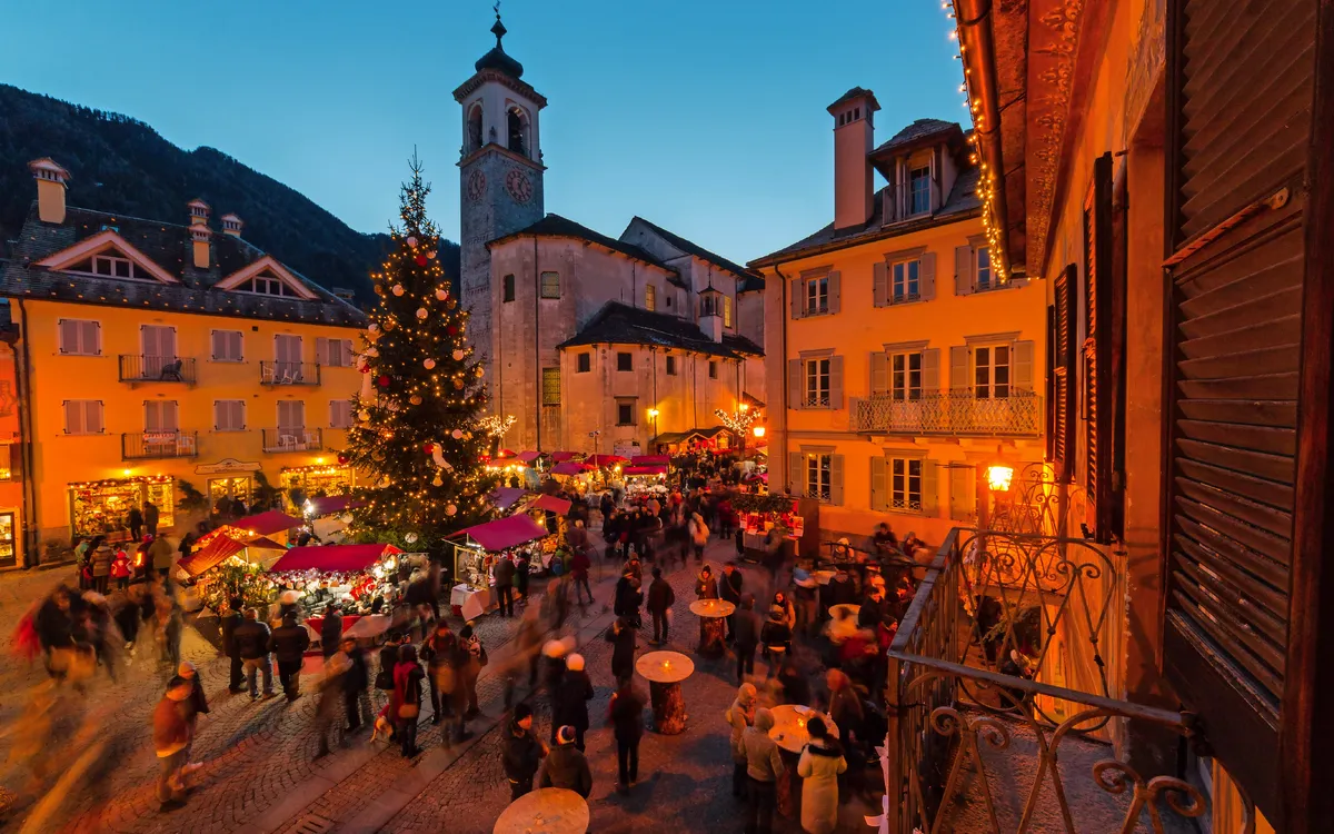 Weihnachtsmarkt mit Menschen und Baum auf beleuchtetem Platz am Abend
