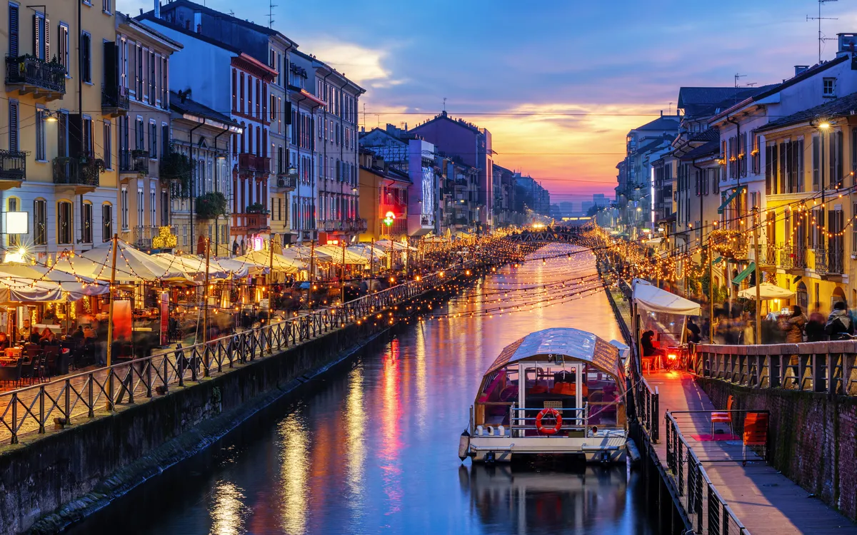 Kanal mit Booten und beleuchteten Cafés in einer Stadt bei Abenddämmerung.