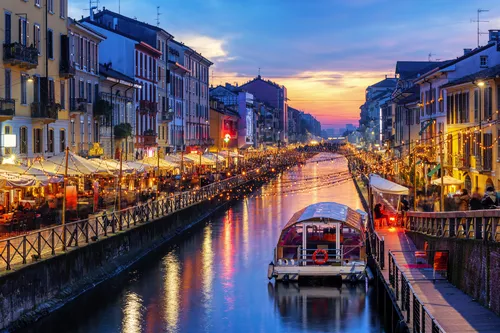 Kanal mit Booten und beleuchteten Cafés in einer Stadt bei Abenddämmerung.