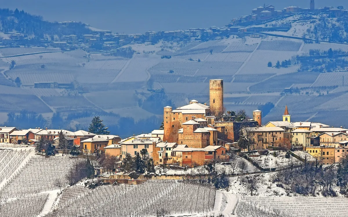 Verschneites italienisches Dorf in hügeliger Landschaft mit mittelalterlicher Burg.