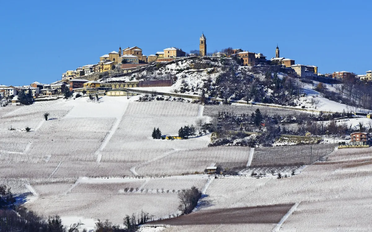 Schneebedecktes Dorf auf einem Hügel mit blauem Himmel im Hintergrund.