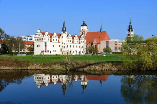 Schloss und Kirche spiegeln sich in einem Fluss bei klarem Himmel.