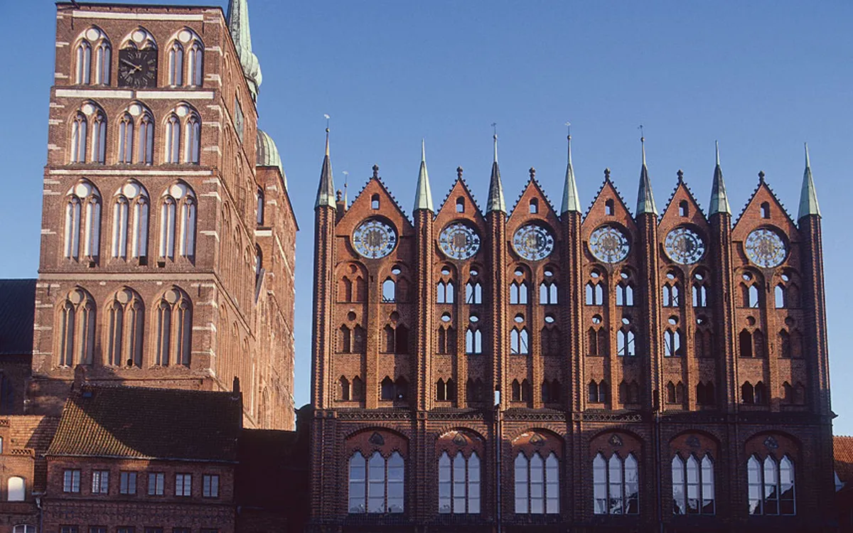 Backsteingotik-Rathaus mit Turm und verzierten Fassaden im Sonnenschein.