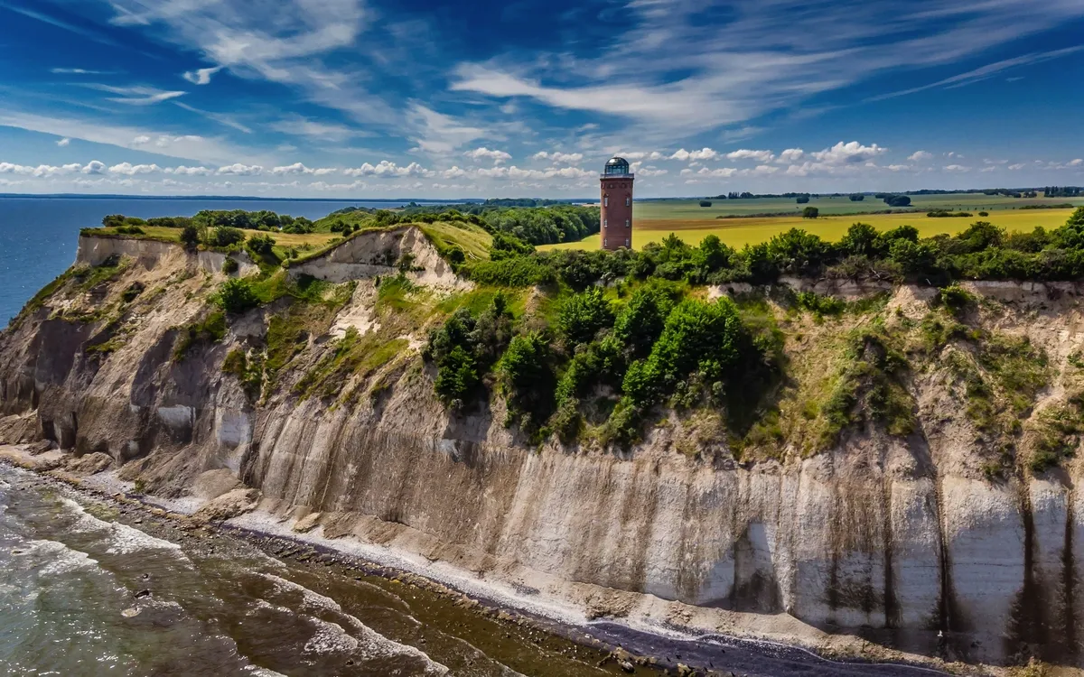 Klippenlandschaft mit Leuchtturm und bewölktem Himmel am Meer.