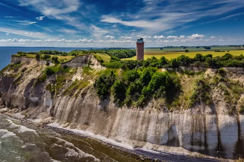 Klippenlandschaft mit Leuchtturm und bewölktem Himmel am Meer.