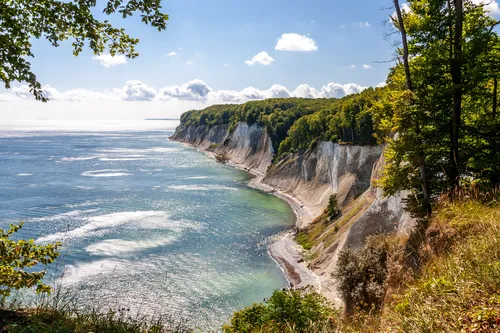 Kreidefelsen am Meer mit bewaldeter Küste und blauem Himmel.