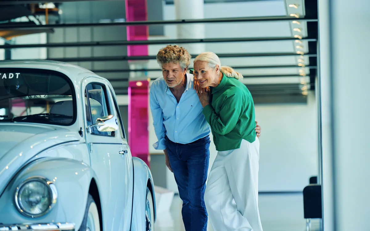 Eine Frau und ein Mann betrachten interessiert ein blaues Auto im Museum.