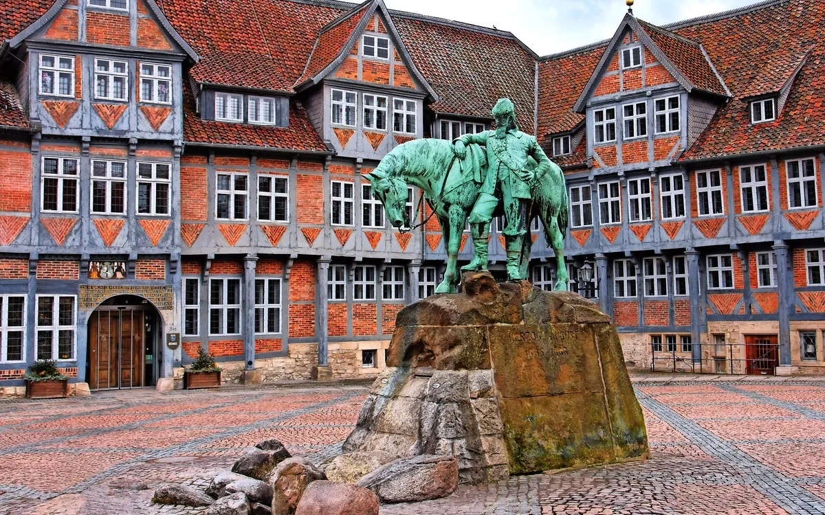 Reiterstatue vor einem historischen Fachwerkgebäude auf einem gepflasterten Platz.