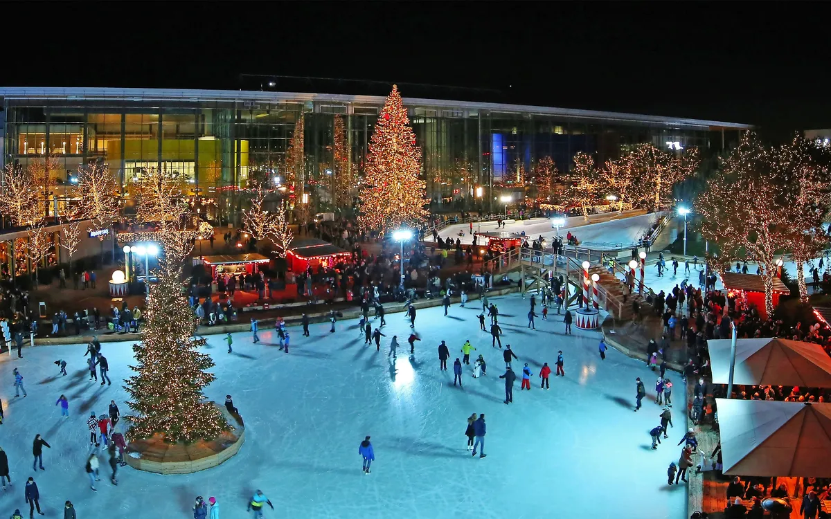 Menschen eislaufen in einer festlich beleuchteten Winterlandschaft bei Nacht.
