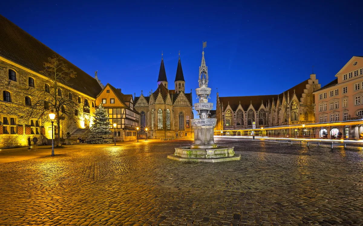 Historischer Platz bei Nacht mit beleuchteten alten Gebäuden und einem Brunnen im Vordergrund