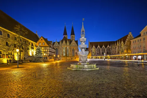 Historischer Platz bei Nacht mit beleuchteten alten Gebäuden und einem Brunnen im Vordergrund