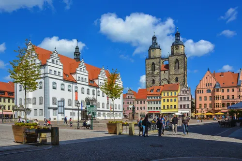 Historischer Marktplatz mit alten Gebäuden und Menschen unter blauem Himmel.