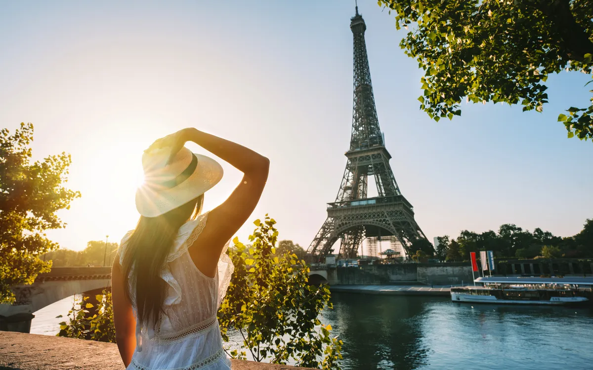 Frau im Sonnenhut vor Eiffelturm bei Sonnenuntergang in Paris