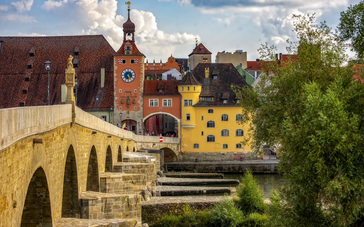 Steinerne Brücke und historische Gebäude in Regensburg bei bewölktem Himmel.