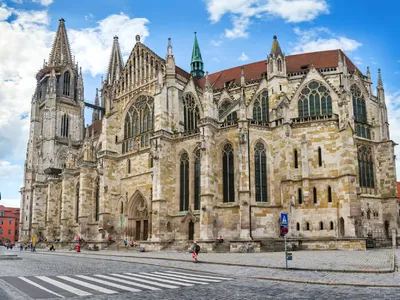 Gotische Kathedrale bei blauem Himmel mit Personen auf einer Kopfsteinpflasterstraße.