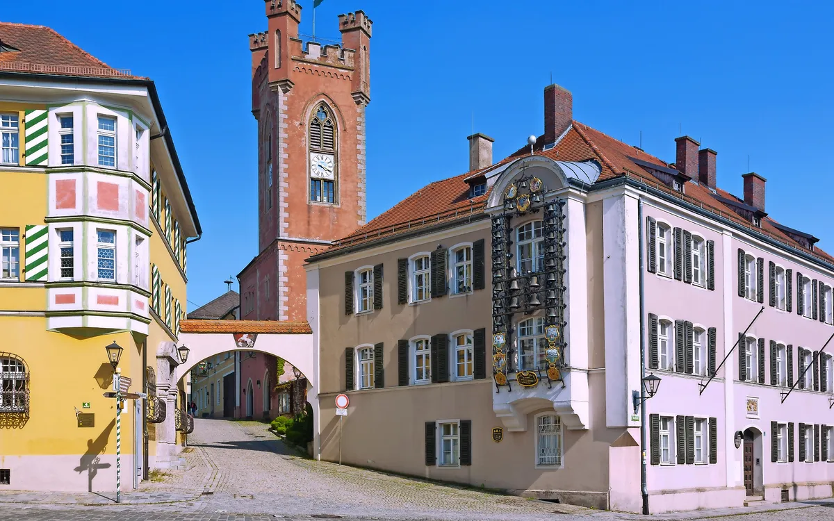 Historischer Platz mit alten Gebäuden und einem Turm bei klarem Himmel.