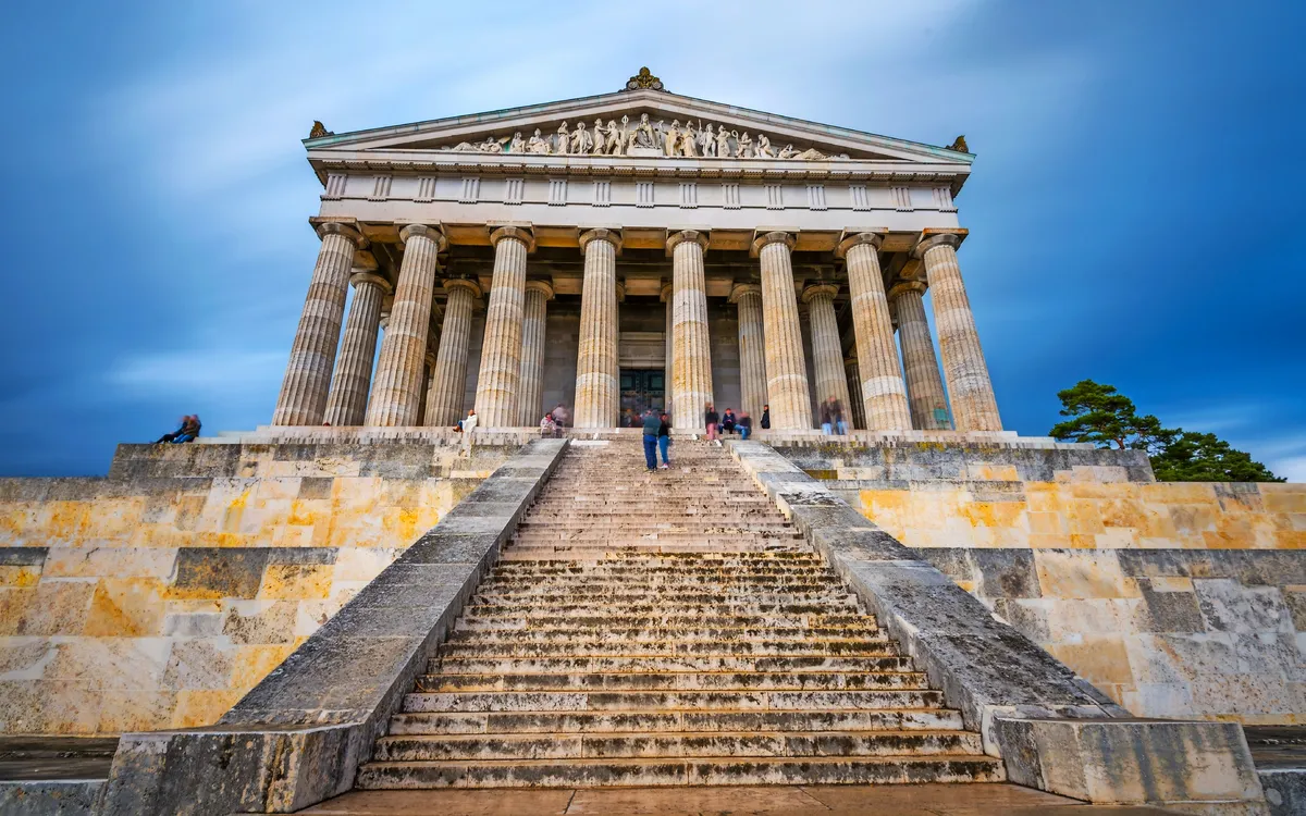 Treppenaufgang zu einem historischen Gebäude mit Säulen und Reliefs.