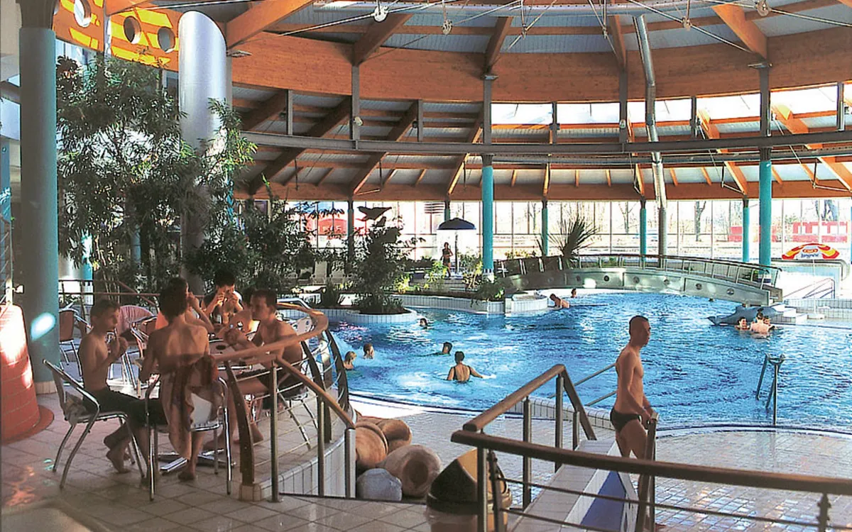 Personen entspannen im Hallenbad mit Pflanzen und großer Glasfassade.